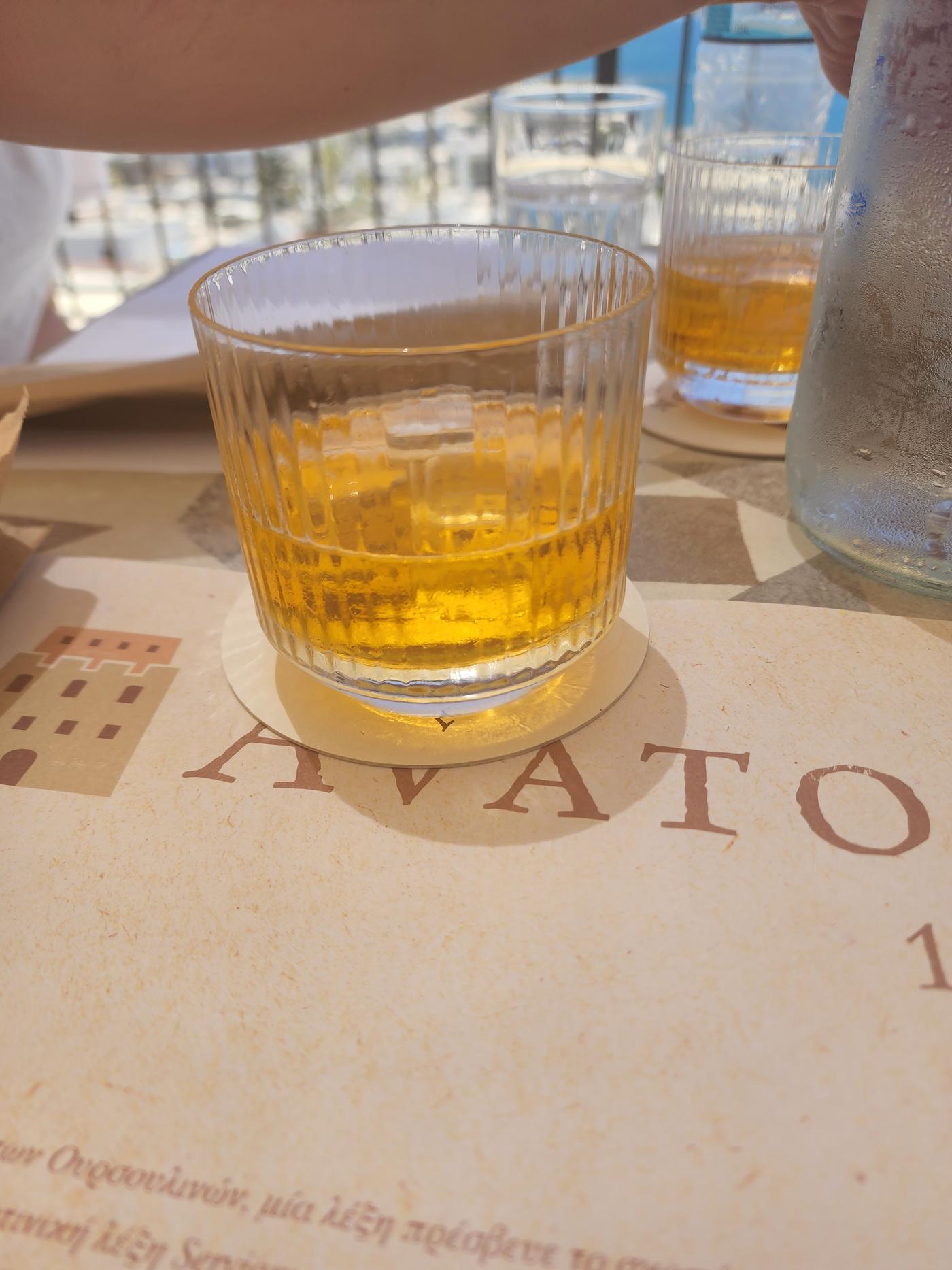 A ribbed glass of golden kitron liqueur on a paper placemat in the sun