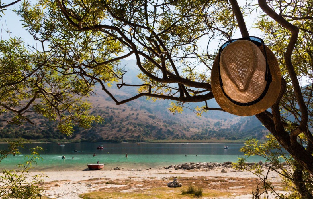 A sun hat hanging from a tree branch above the turquoise water of Lake Kournas