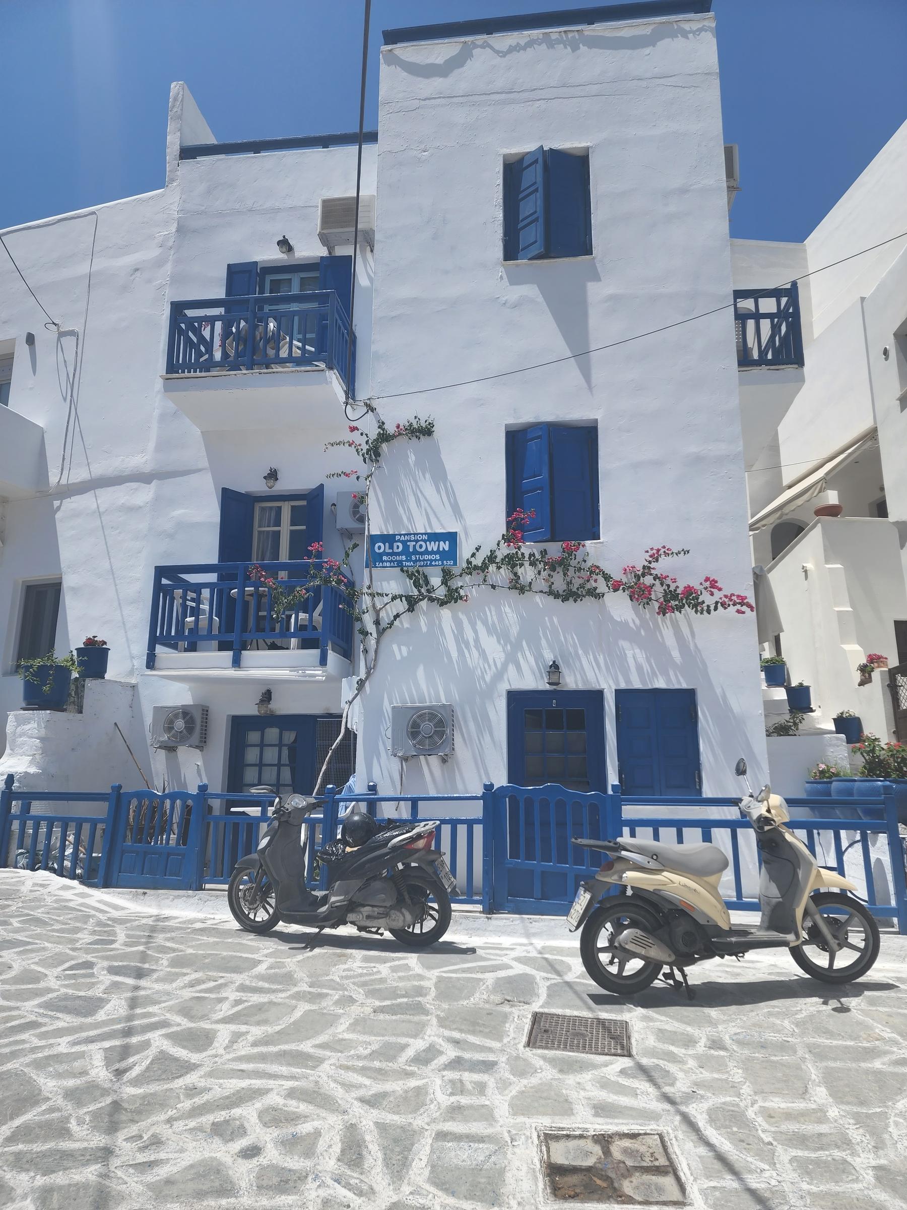 A whitewashed Naxos guesthouse with blue balconies and shutters, bougainvillea climbing the wall