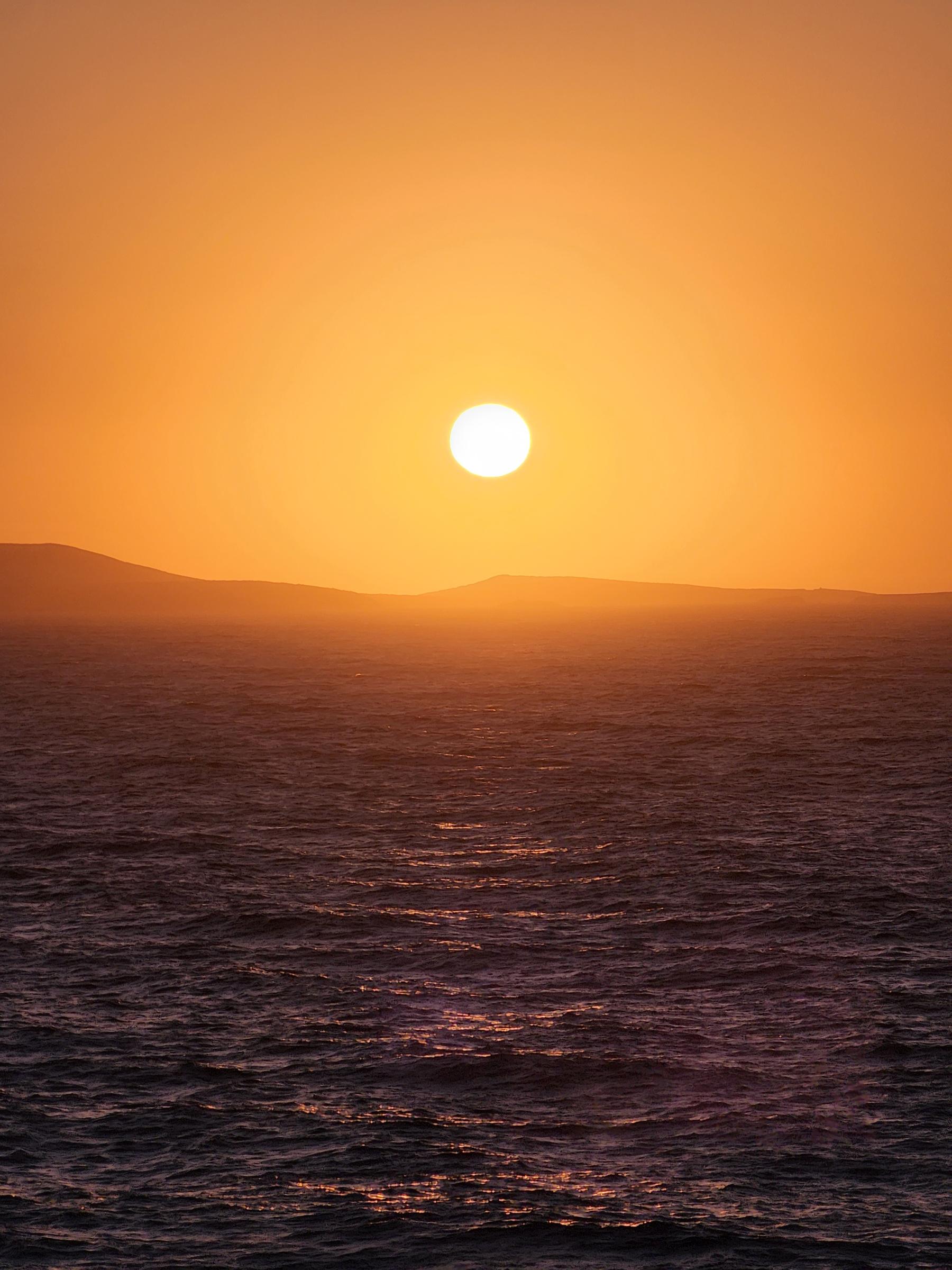 A huge orange sun sinking toward the dark Aegean, an island silhouetted on the horizon