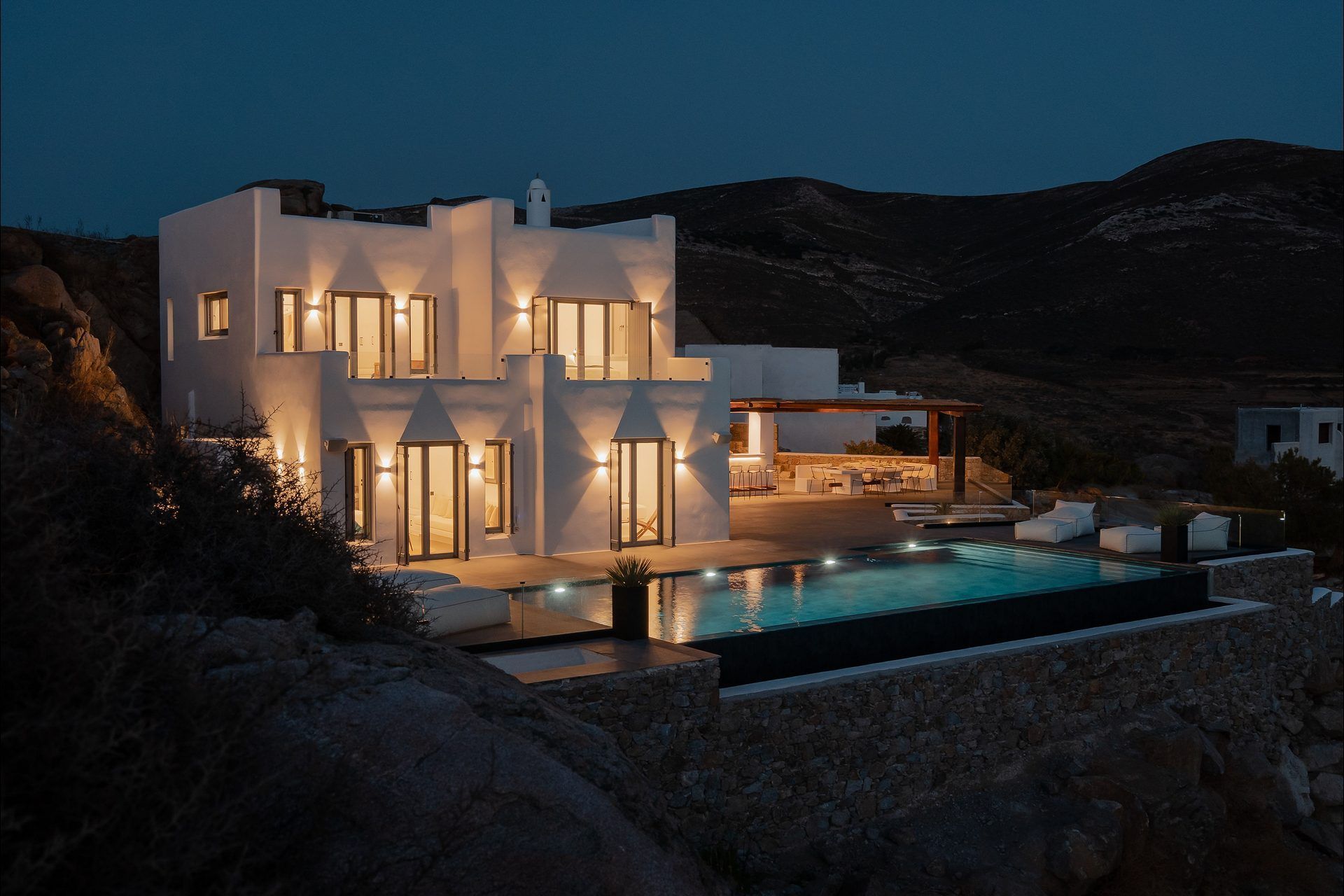 The villa at night, its windows and terrace lit gold beside the illuminated pool