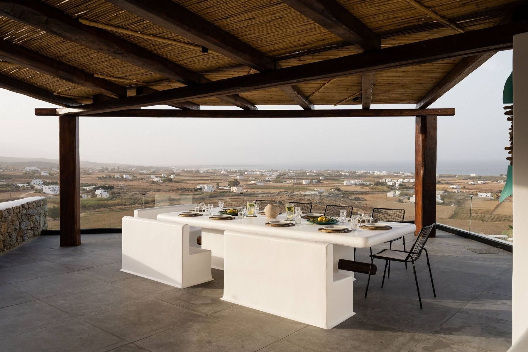 A long whitewashed dining table under a reed pergola, looking out over Naxos's fields to the sea